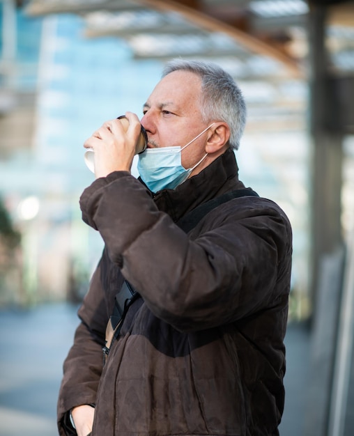 Covid-Coronavirus-Konzept maskierter reifer Mann, der im Freien Kaffee trinkt