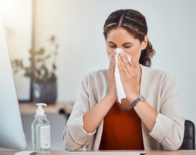 Covid doente e mulher assoando o nariz com um lenço enquanto trabalhava em seu escritório moderno durante a pandemia Gripe resfriado ou alergia sinusal espirro de menina do méxico sentada em sua mesa com problemas de saúde