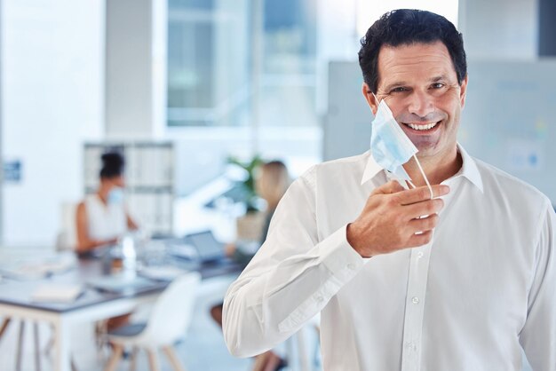 Covid-Gesundheits- und Freiheitsmaske für Mann im Büro nach Sperrung Porträt eines glücklichen Geschäftsmannes, der eine Gesichtsmaske aufsetzt, um die Ausbreitung des Virus am Arbeitsplatz einzudämmen und die Mitarbeiter vor Infektionen zu schützen