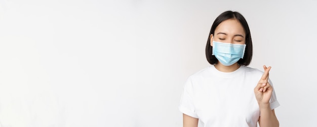 Covid-Gesundheits- und medizinisches Konzeptbild eines asiatischen Mädchens in medizinischer Gesichtsmaske, das die Finger betet