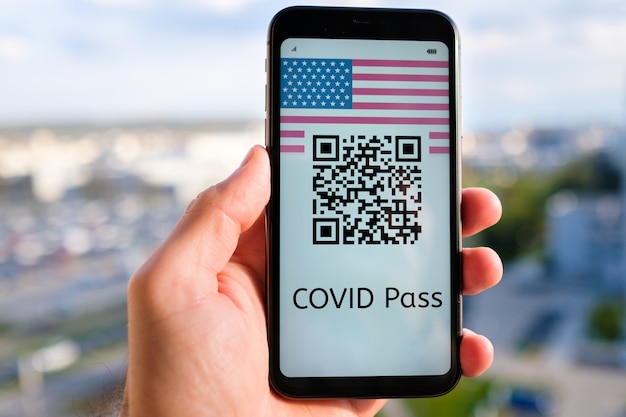 Covid pass con código qr con bandera de estados unidos en la pantalla del teléfono inteligente en la mano del hombre en el fondo de