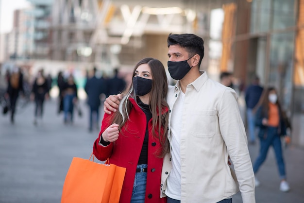 Covid- und Coronavirus-Einkaufspaar, das in einer Stadt spazieren geht, während es Einkaufstaschen trägt