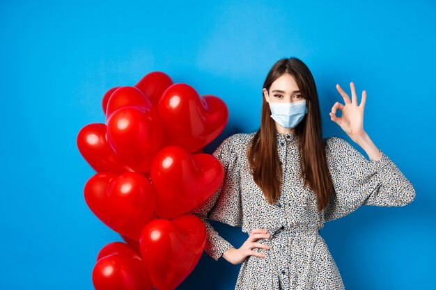 Covid-Valentinstag und Pandemie-Konzept schöne junge Frau in Gesichtsmaske und Kleid, die ok...