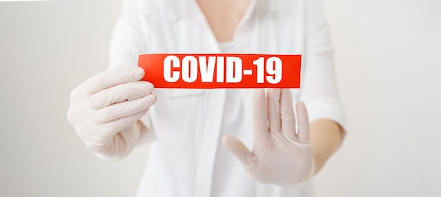 COVID19 Coronavirus, señal de advertencia roja con el texto COVID19 en manos de médico con bata blanca, guantes, mascarilla médica.