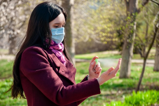 COVID19. Junge Frau im Schutz sterile medizinische Gesichtsmaske im Freien Sprays Hände Desinfektionsmittel. Coronavirus-Konzept.