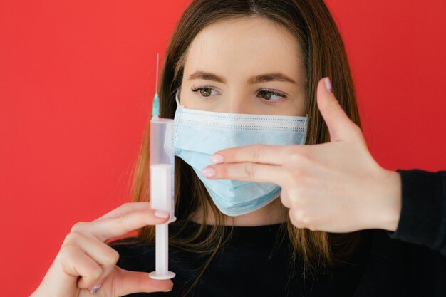 Foto covid19 pandemic coronavirus jovem garota com máscara facial de fundo vermelho protetora segurando uma seringa c