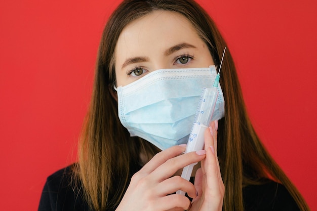 COVID19 Pandemic Coronavirus Jovem garota com máscara facial de fundo vermelho protetora segurando uma seringa C