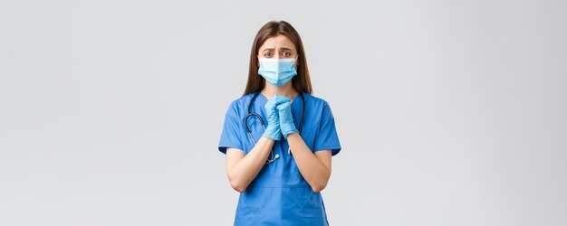 Covid19 verhindert Virus-Gesundheitspersonal und Quarantänekonzept Hoffnungsvolle verzweifelte Krankenschwester in blauen Scrubs, die die Menschen bitten, während der Pandemie Coronavirus zu Hause zu bleiben, halten die Hände im Gebet