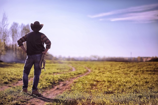 Cowboy in einem Hut und mit einem Lasso, das in einem Feld bei Sonnenuntergang stehtxA