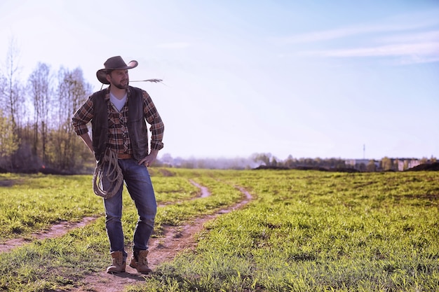 Cowboy mit Hut und Lasso, der bei Sonnenuntergang auf einem Feld steht