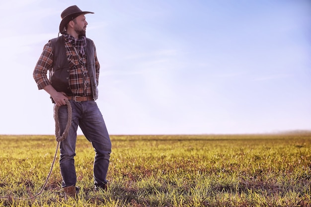 Cowboy mit Hut und Lasso, der bei Sonnenuntergang auf einem Feld steht