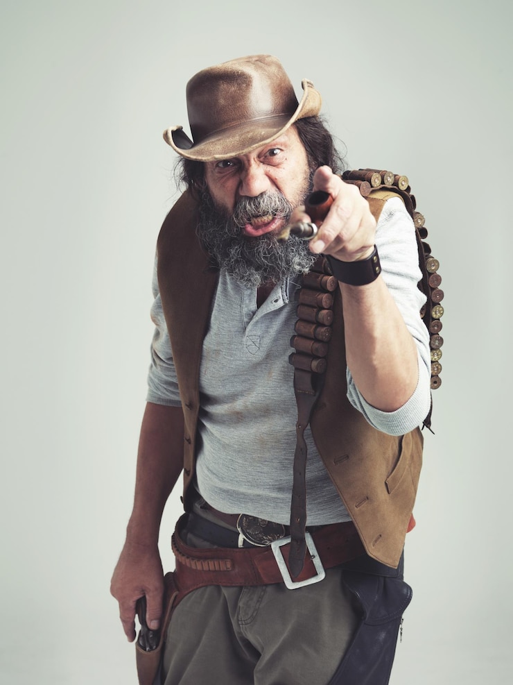 Foto cowboy sênior aponta e cara zangada em estúdio traje e baú para retrato ocidental olhando desleixado velho homem chapéu de xerife e homem sujo para texas fundo cinzento e gesto irritado para fora da lei