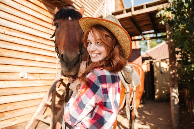 Cowgirl alegre e bonita jovem com seu cavalo no rancho