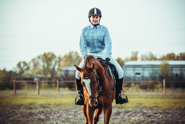 Cowgirl com um chapéu em pé perto de um cavalo em um campo