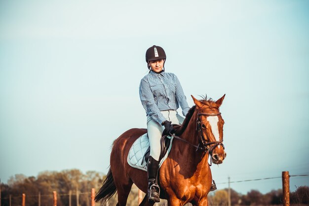 Cowgirl mit Hut steht neben einem Pferd auf einem Feld