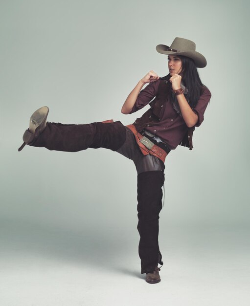 Foto cowgirl patear y pelear con los puños en el estudio para el personaje del oeste salvaje traje y sombrero para el alguacil persona femenina disfraz y enojado con agresión rabia y aislado con fondo gris