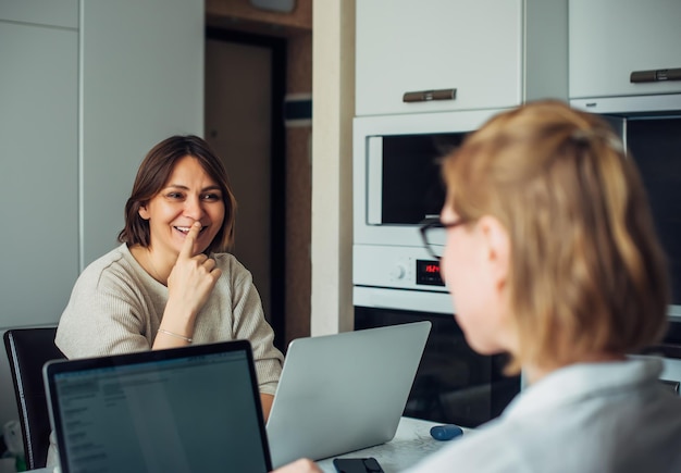 Foto coworking remote work home office startup zwei junge hübsche frauen, die mit einander zugewandten laptops sitzen, konzentrieren sich auf das brünette gesicht