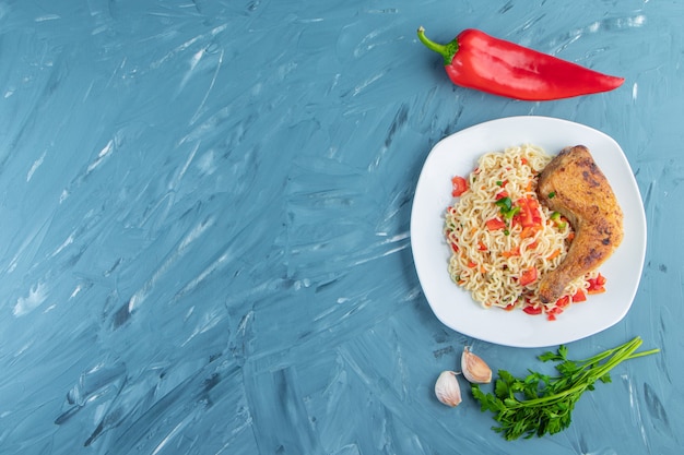 Coxa de frango e macarrão em um prato ao lado de legumes, no fundo de mármore.