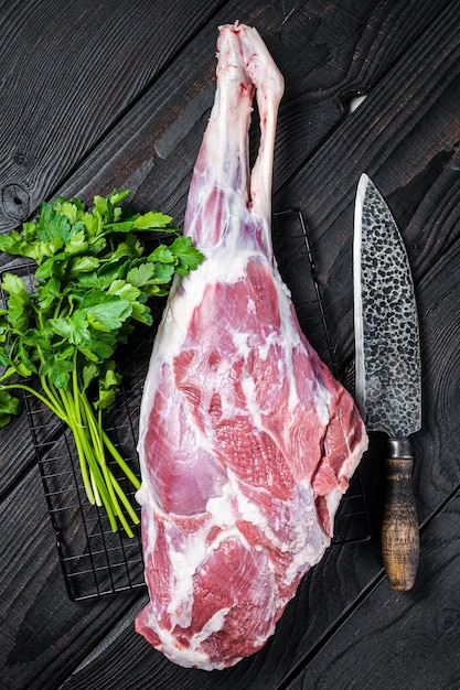 Coxa de perna de carneiro fresca e crua na mesa da cozinha com ervas Fundo de madeira preta Vista superior