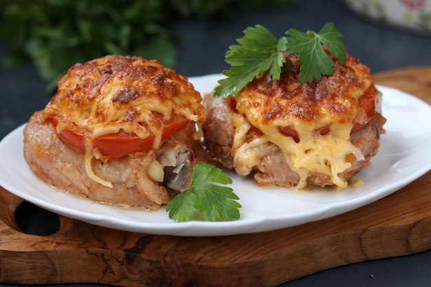 Coxas de frango com tomate e queijo, dispostas em um prato sobre uma tábua de madeira