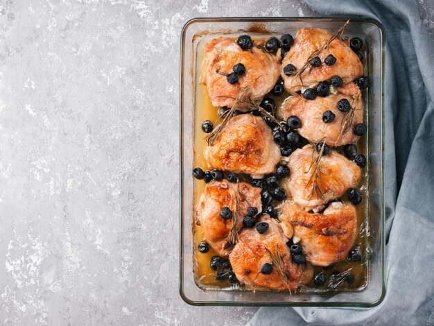 Coxas de frango corsos com alecrim, azeitonas pretas, alho em suco de limão e vinho. Pernas de frango cozidas no forno em fundo cinza de concreto. Coxa de frango assada em vidro à prova de calor. Vista superior.