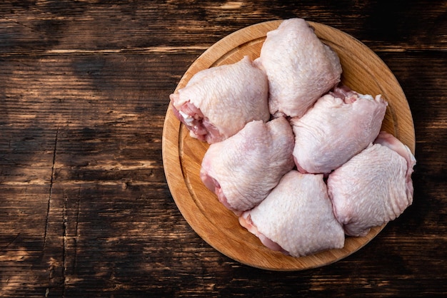 Coxas de frango cru na placa de madeira em fundo escuro de madeira.