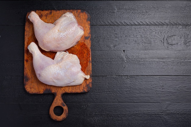 Coxas de frango cru na superfície de madeira escura.