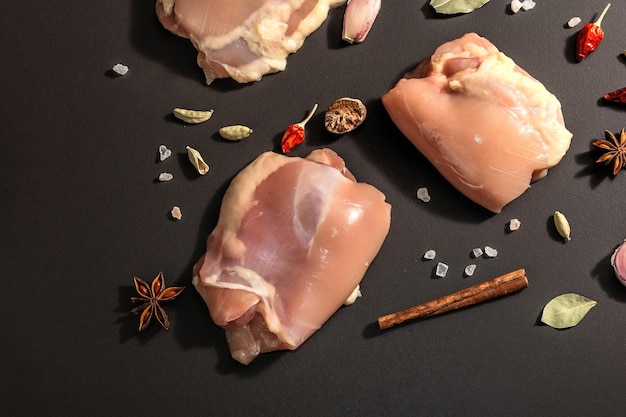 Coxas de frango cruas sem ossos ou pele. Um ingrediente útil para preparar alimentos saudáveis, especiarias, alho. Fundo de pedra preta, luz dura na moda, sombra escura, vista superior