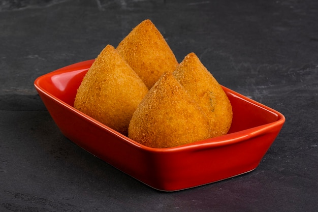 Coxinha frita tradicional en un recipiente rojo sobre una piedra de pizarra.