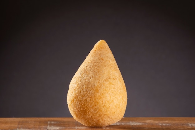 Coxinha frito en mesa de madera con fondo degradado marrón.