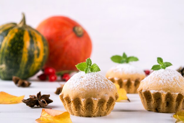 Cozimento caseiro em estilo outono. bolinhos deliciosos em uma placa de madeira com paus de canela, estrelas de anis, abóboras e bagas de rosa mosqueta. na mesa branca