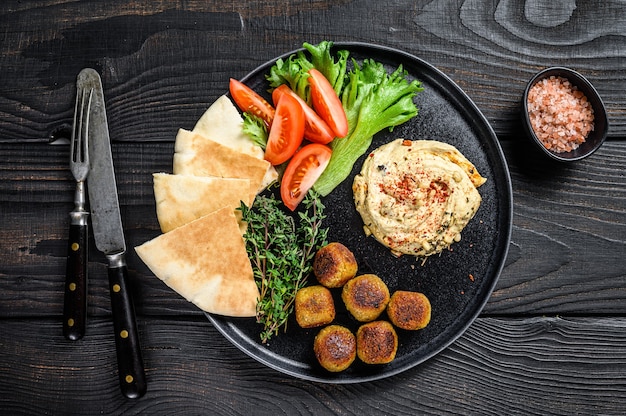 Cozinha árabe Hummus grão-de-bico, falafel, pão sírio e legumes frescos. Fundo de madeira preto. Vista do topo.