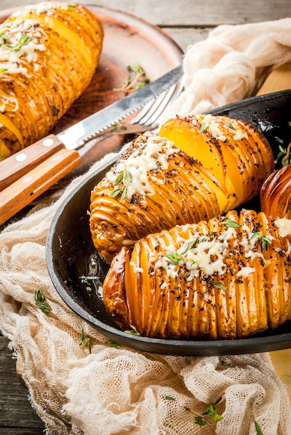 Foto cozinha caseira tradicional americana. a dieta vegana. batata caseira hasselback com ervas frescas e queijo. na mesa de madeira velha, copie o espaço