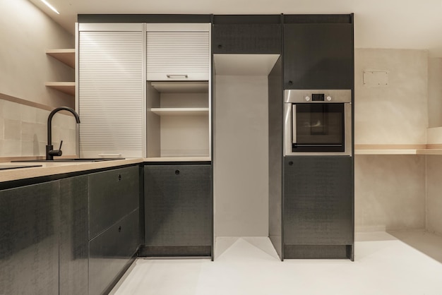 Cozinha com móveis verdes, armário preto com persianas de alumínio e espaço vazio para a geladeira