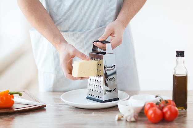 Cozinha, comida e conceito de casa - close-up de mãos masculinas ralar queijo