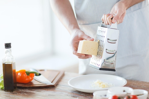 cozinha, comida e conceito de casa - close-up de mãos masculinas ralar queijo