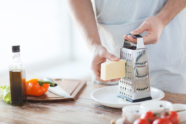 cozinha, comida e conceito de casa - close-up de mãos masculinas ralar queijo