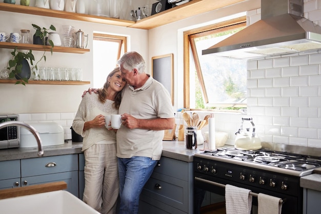 Cozinha de amor e casal sênior relaxam com uma xícara de café, chá ou bebida quente enquanto se unem e se conectam em casa Paz familiar e homem e mulher idosos desfrutam de tempo de qualidade aposentadoria e vida juntos