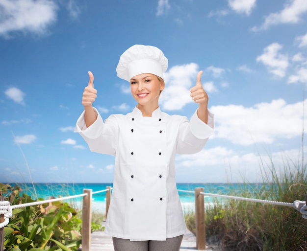 Cozinha, gesto e conceito de comida - sorridente chef feminina, cozinheira ou padeiro mostrando os polegares para cima