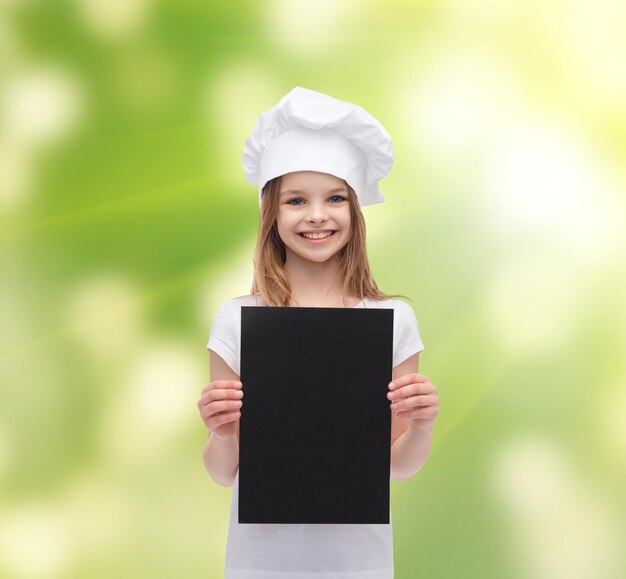 cozinha, infância, ecologia, propaganda e conceito de pessoas - sorridente chef menina ou padeiro com papel preto em branco sobre fundo verde