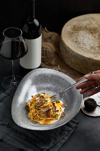 Cozinha italiana - espaguete com trufa preta em um prato cinza e uma garrafa de vinho. Foco seletivo. Vertical.