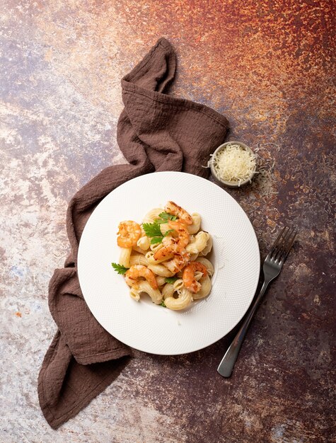 Cozinha italiana. macarrão com molho bechamel com camarão verde, queijo e salsa no prato enquanto no fundo escuro, vista superior copie o espaço