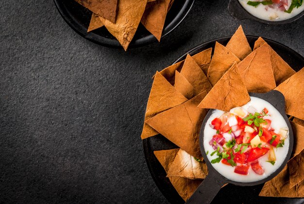 Cozinha mexicana, latino-americana. receita queso blanco - cream cheese, creme, legumes frescos, tomates, cebola, pimentão, ervas. com tortilhas assadas, mesa de pedra preta. vista superior copyspace