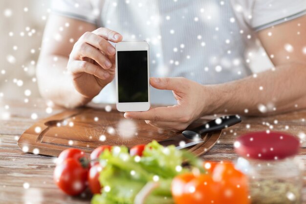 cozinha, pessoas, tecnologia e conceito de casa - closeup de homem com legumes na mesa mostrando a tela do smartphone em branco na cozinha