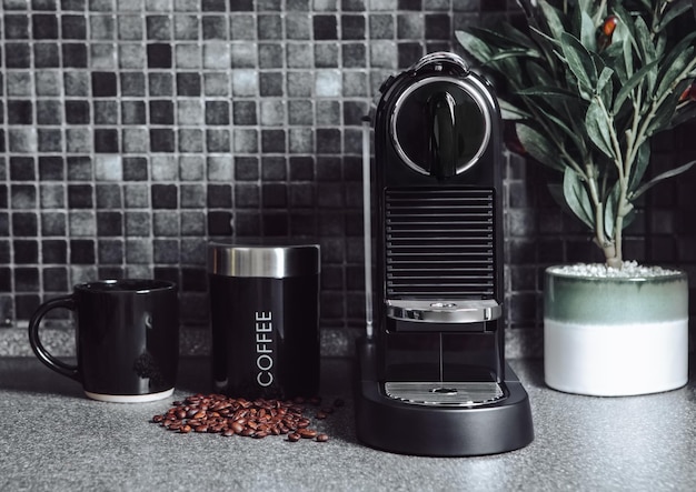 Cozinha preta com máquina de café caseira e feijão com xícara e planta de oliveira