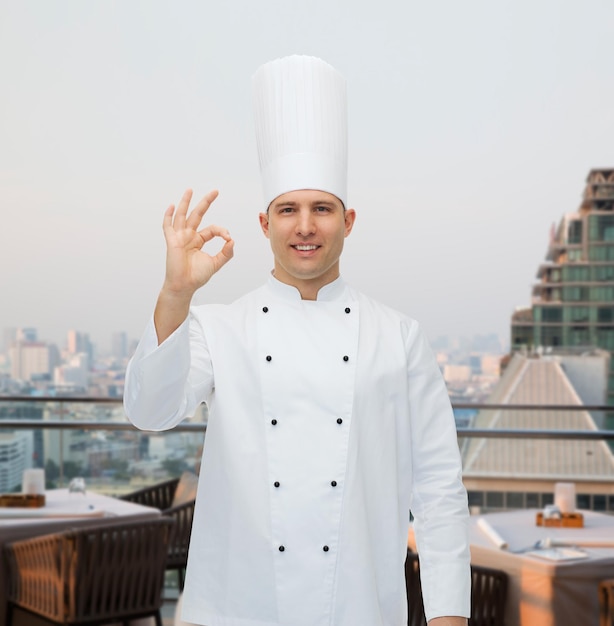 cozinha, profissão, gesto e conceito de pessoas - cozinheiro chef masculino feliz mostrando sinal ok sobre o fundo do salão do restaurante da cidade