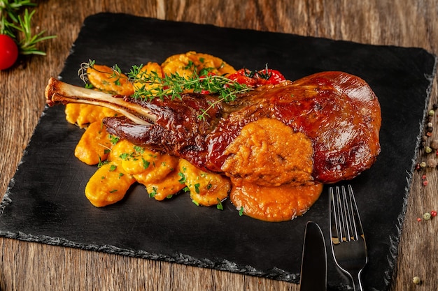 Cozinha sérvia, balcânica. Cordeiro de perna com nhoque. Servindo em um restaurante em uma lousa preta, em uma mesa de madeira