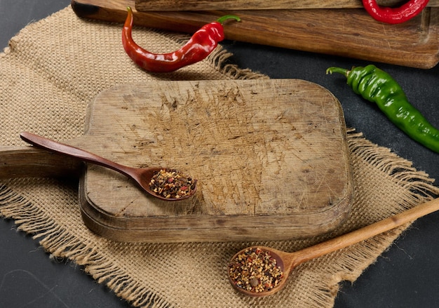 Cozinha vazia tábua de madeira marrom na mesa preta, ao lado de colheres com especiarias e pimenta fresca, fundo preto