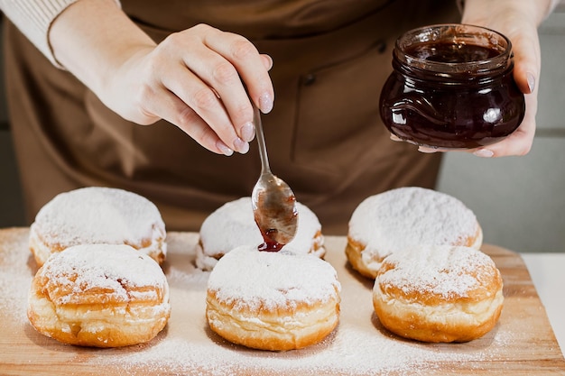 Cozinhando o sufganiyot tradicional de Hanukkah Mulher decora rosquinhas com geleia Sobremesa festiva judaica