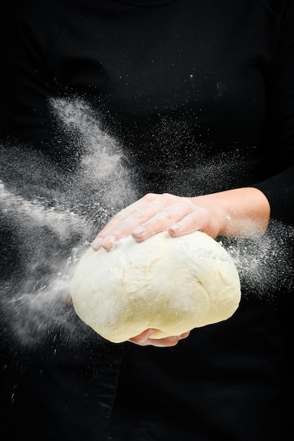 Cozinhar a massa pelas mãos do chef para pão de pastelaria caseiro com respingo de farinha em um fundo escuro